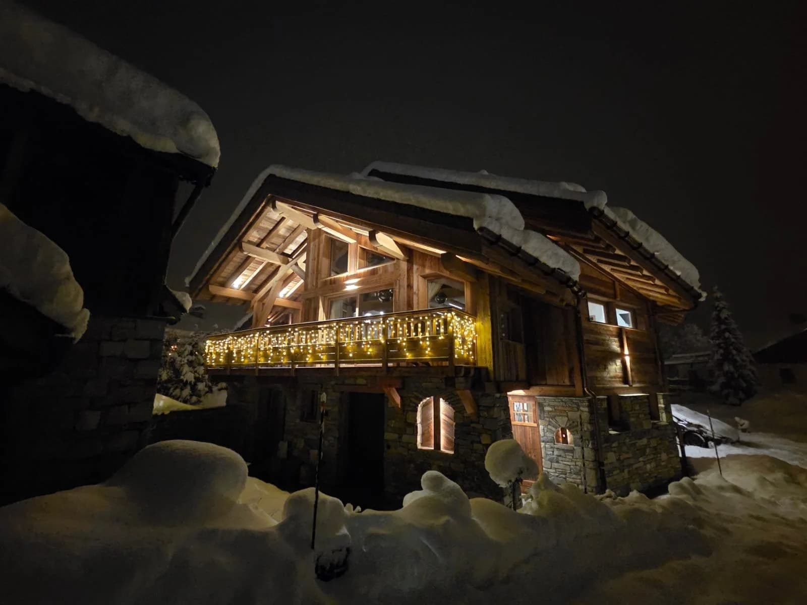 The chalet at night, its balcony strung with fairy lights above deep snow