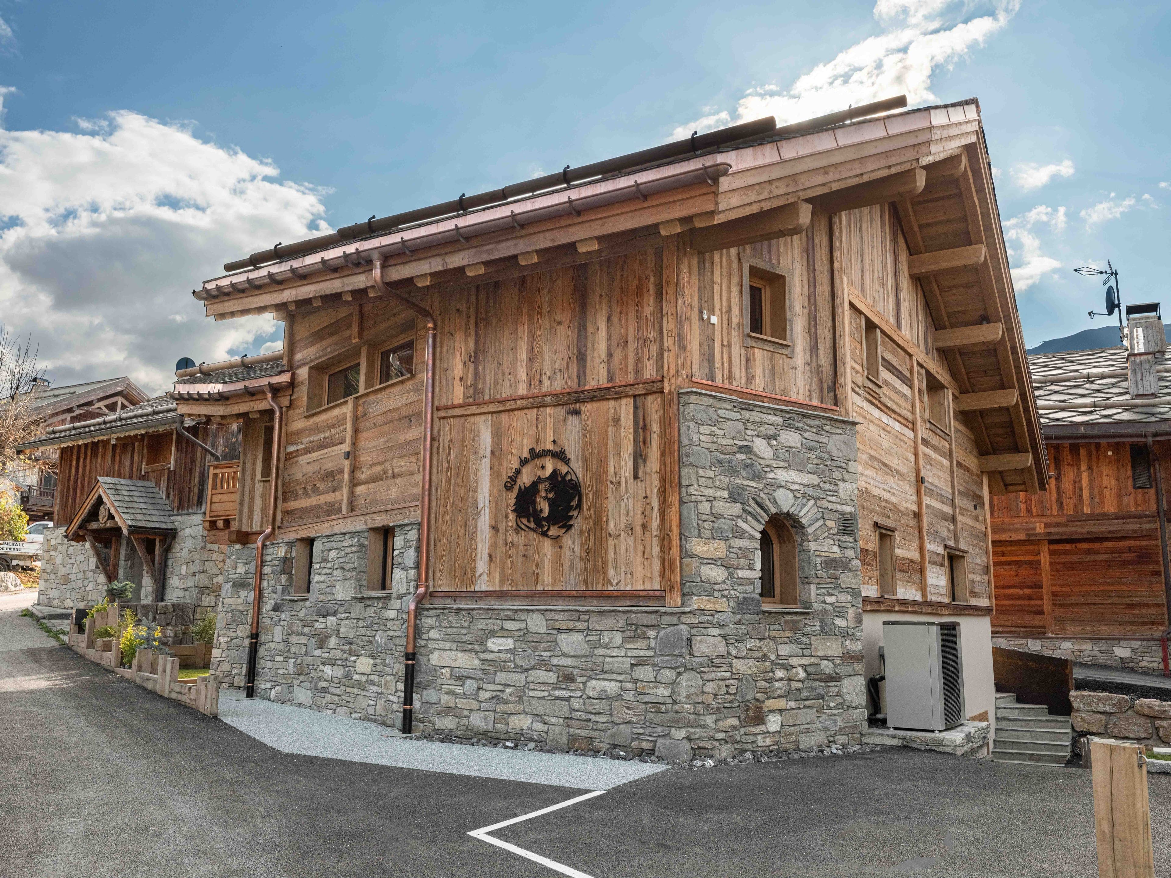 The chalet in summer: timber and stone façade with the marmot emblem